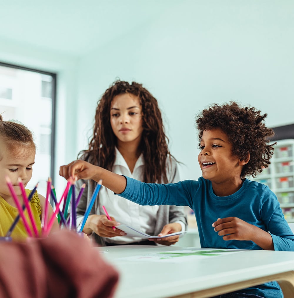 A boy smiling during an ABA therapy session, engaging in a hands-on activity with colorful materials, alongside another child and a therapist in a structured learning environment